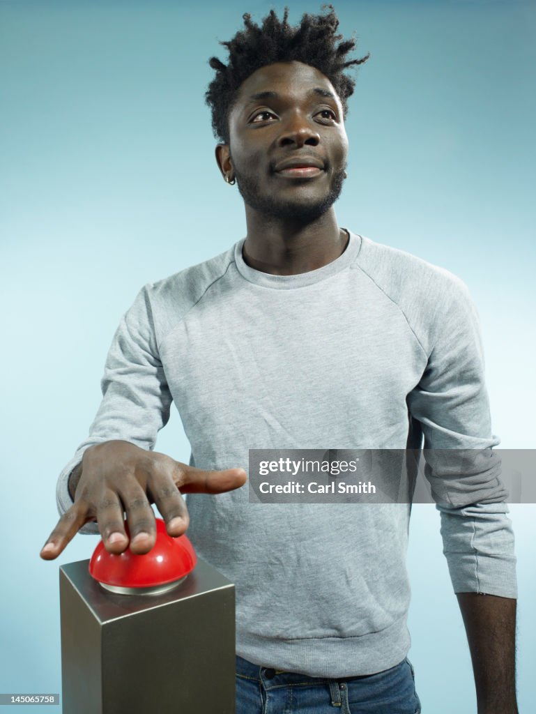 A hip young man with his hand poised above a red game show buzzer