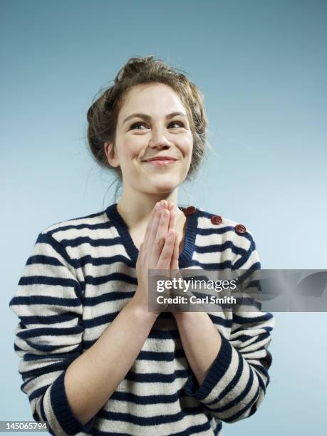 a young woman with her hands together with a look of excited hope - pleading stock pictures, royalty-free photos & images
