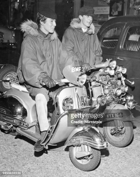 Two Mods sit on their scooters wearing fur collared Parka coats. The bikes are covered with spot lights, a mod fashion statement. 24th October 1963.
