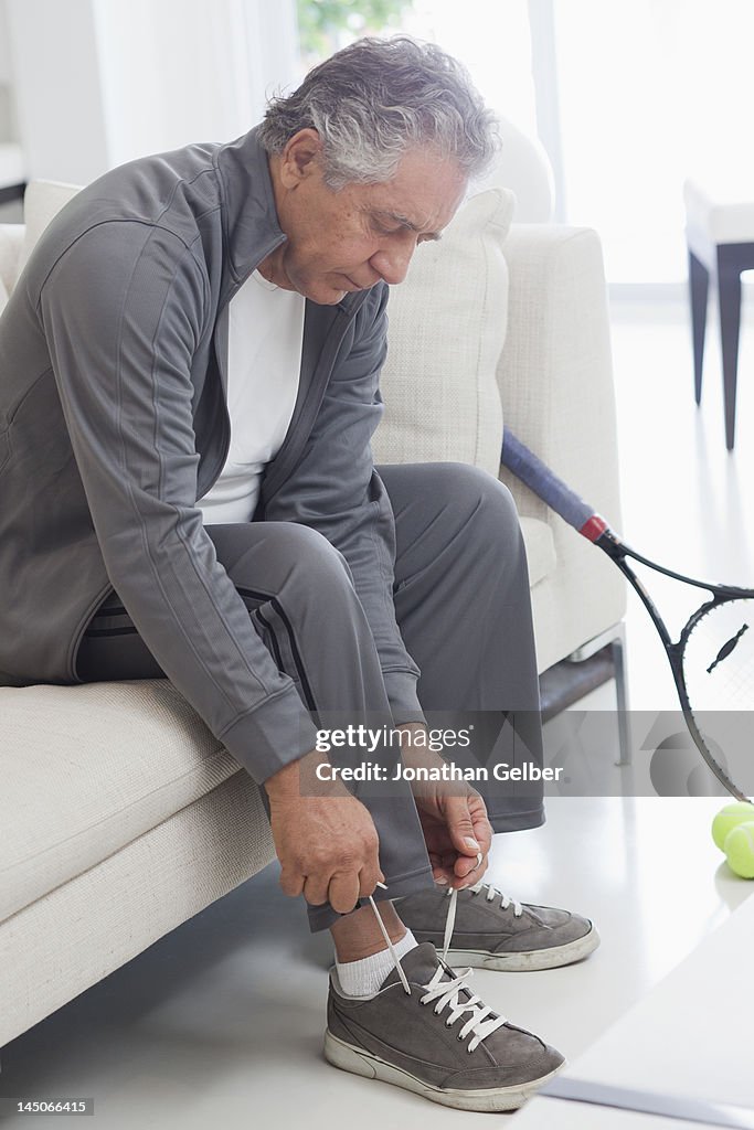 A senior man tying his shoelaces, preparing to play tennis