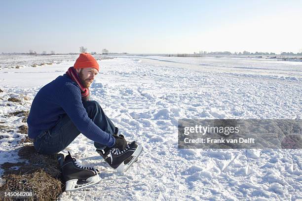 man lacing up ice skates in snowy field - hockey skate stock pictures, royalty-free photos & images