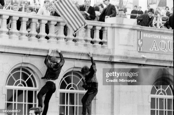 Battle for Brighton 1964. Two rockers cling on to the sides of the building on the beach, as the mods above attempt to through a deckchair onto them....