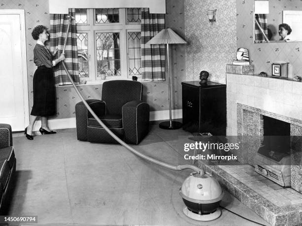 Housewife cleaning the curtains in her living room using the hose from a Hoover Constellation vacuum cleaner. September 1956.