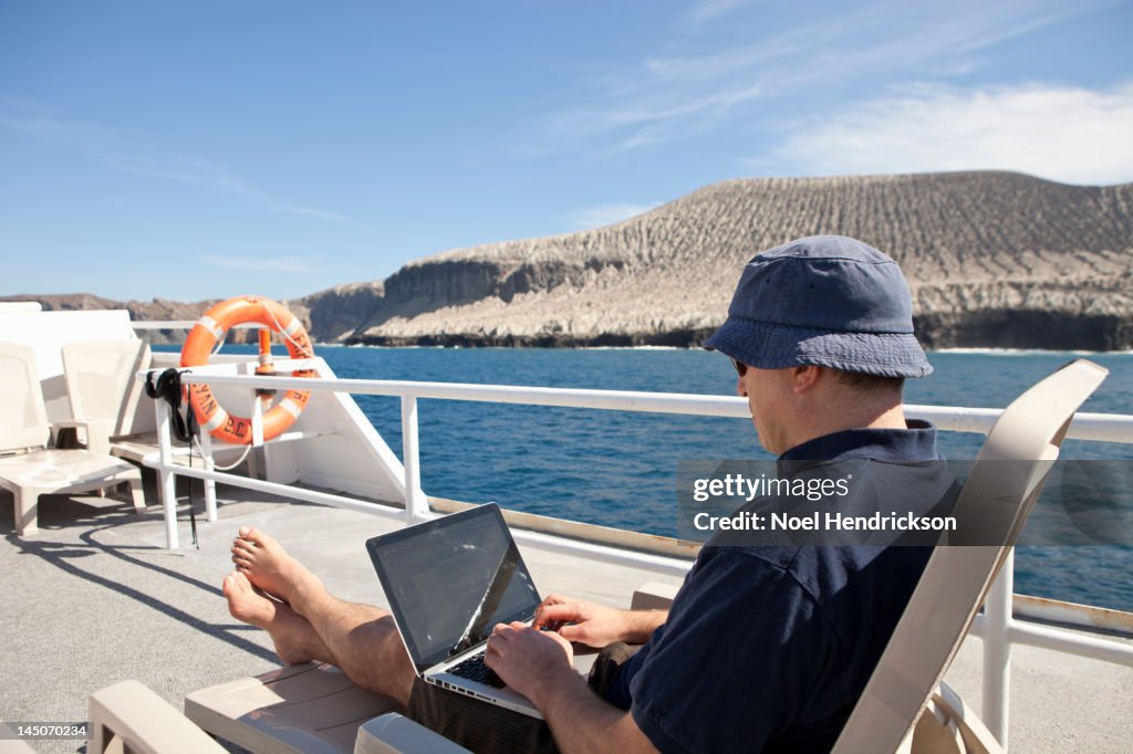 A man on his laptop on the deck of a boat