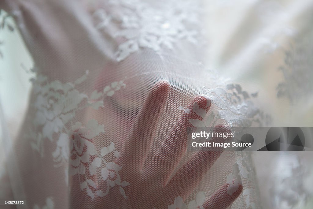 Hand of woman behind lace curtain