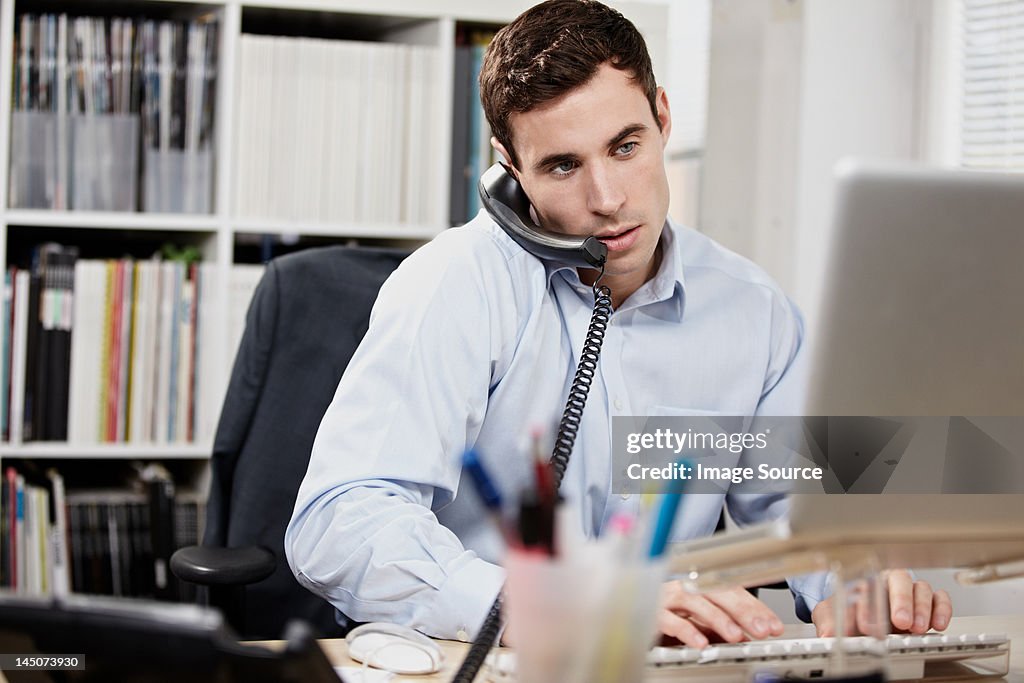 Young man on telephone and working on laptop