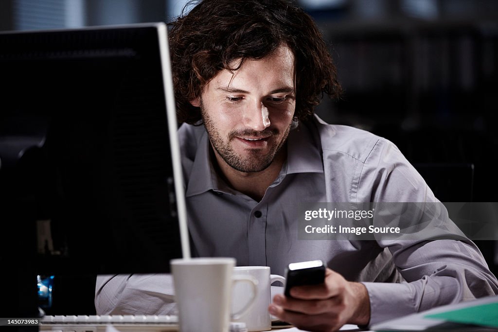 Office worker looking at cellphone in dark office