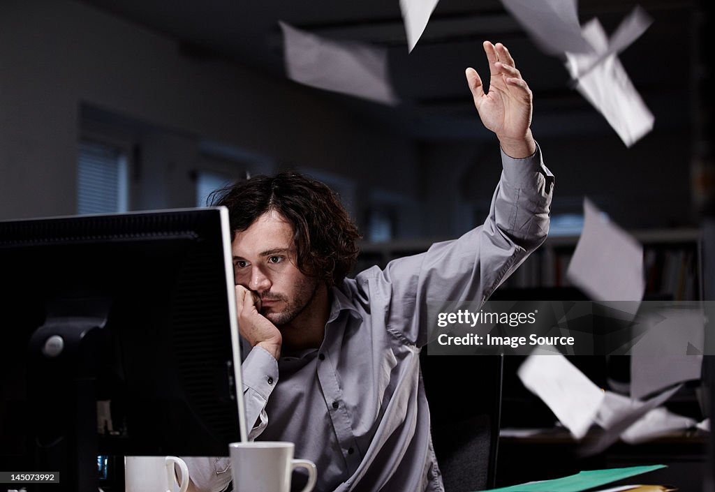 Office worker working late, throwing paper in the air