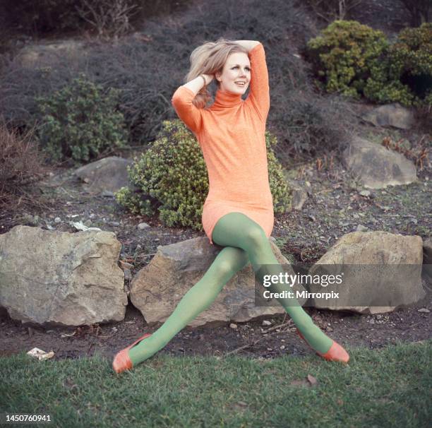 Model wearing full length orange sweater and green matching stockings, sitting on rockFebruary 1968.