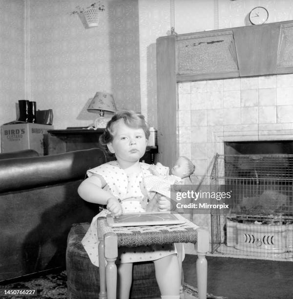 Young Betty Hampson, aged 3, sitting beside the fireplace drawing on a chalk board. July 1957.