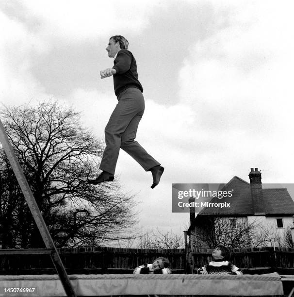 Racing driver Graham Hill at home with children on trampoline in his garden with son Damon and daughter Bridget watching.