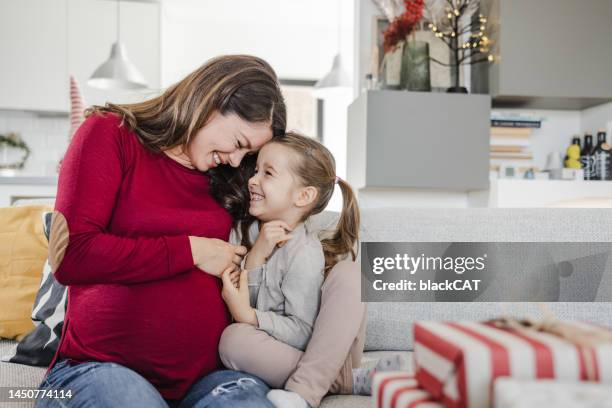 mujer embarazada y su hija abrazándose en casa - baby touching belly fotografías e imágenes de stock