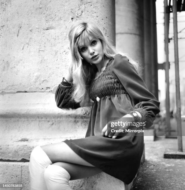 Actress and model Madeline Smith, aged 20, photographed in London wearing a black dress and white knee high boots. November 1969.