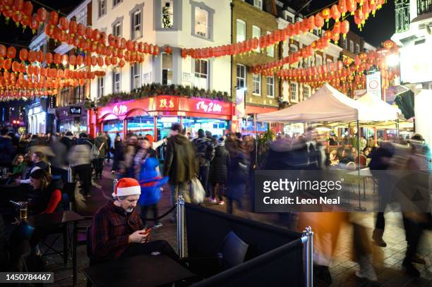 Man wearing a Santa hat checks his phone as Christmas shoppers flow through Chinatown on December 20, 2022 in London, England. The UK's hospitality...