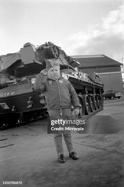 Six year old boy wearing an army cap and badge gives a salute as he stands in front of a British Chieftain Tank. November 1969.