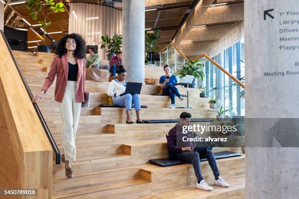 empresária descendo as escadas com colegas trabalhando em degraus no escritório criativo - mover para baixo - fotografias e filmes do acervo