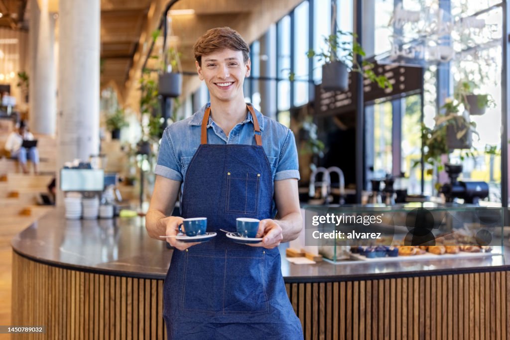 Lächelnder junger Barista serviert zwei Tassen Kaffee in der Bürocafeteria