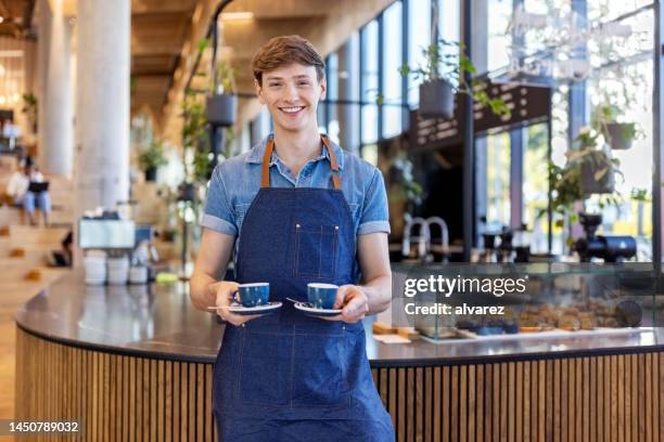 joven barista sonriente sirviendo dos tazas de café en la cafetería de la oficina - camarero fotografías e imágenes de stock