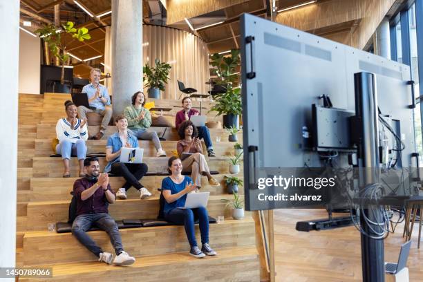 business-team sitzt auf stufen und applaudiert nach einer videokonferenz - telefonkonferenz stock-fotos und bilder