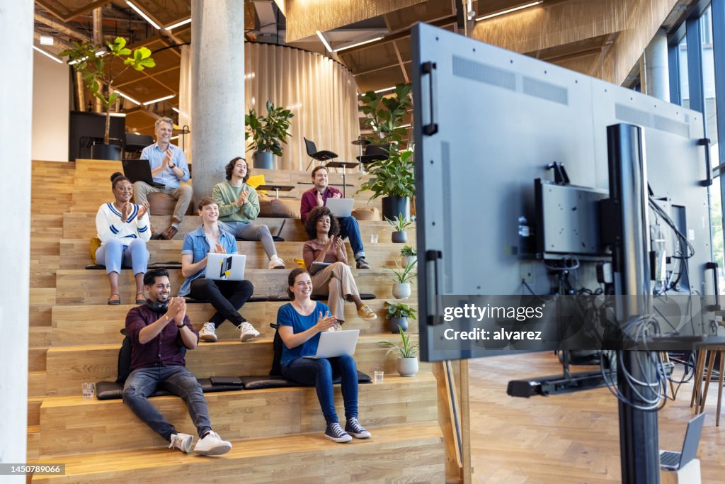 Business team sitting on steps and applauding after a video conference