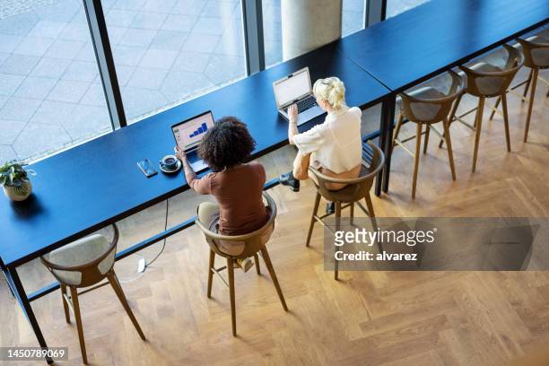 two women at coffee shop working on laptops - ciber café imagens e fotografias de stock