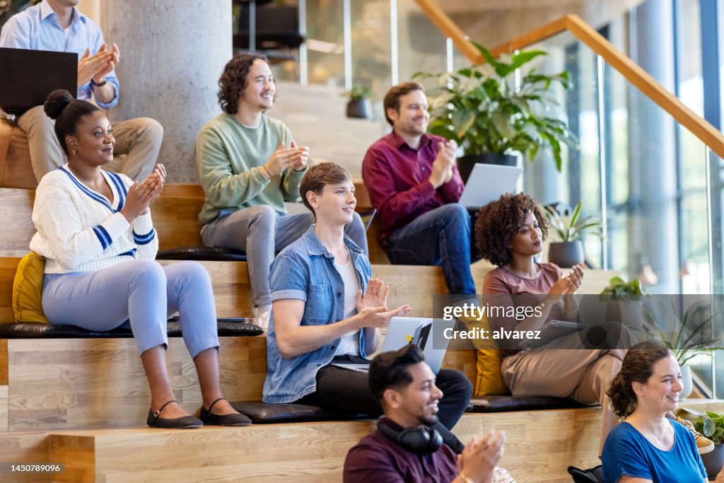 Diverse group of businesspeople sitting on steps clapping hands during a conference