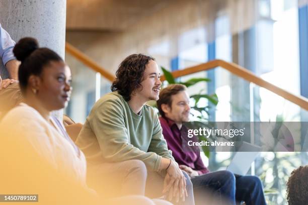happy young man sitting amidst colleagues during a conference - building atrium stock pictures, royalty-free photos & images