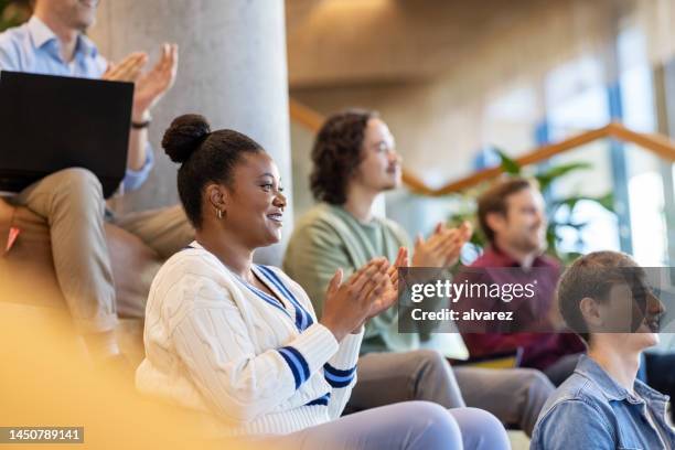 multiethnische gruppe von menschen, die während einer konferenz auf stufen sitzen und in die hände klatschen - african hands clap stock-fotos und bilder