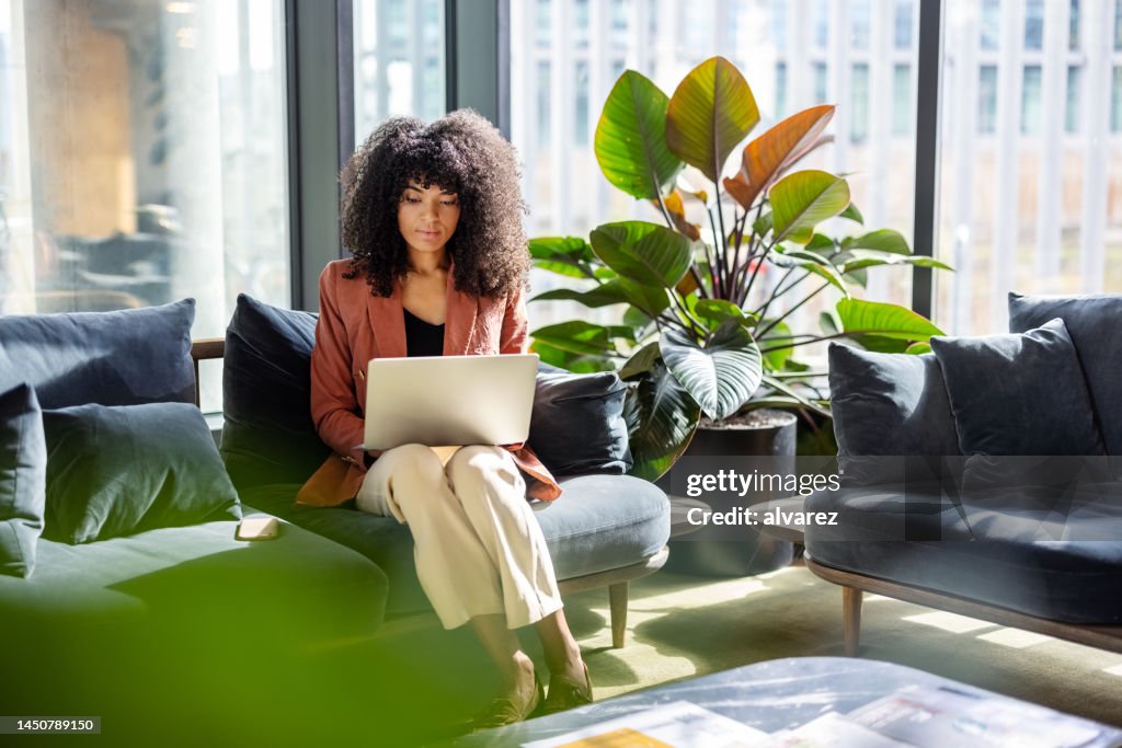Young African woman working on laptop sitting at office lobby