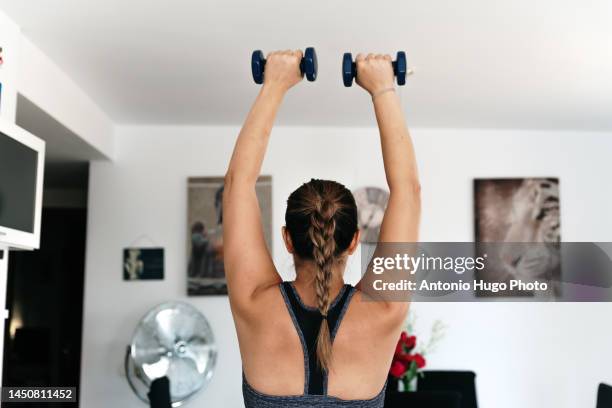 woman on her back exercising with dumbbells in her living room. - leggings imagens e fotografias de stock