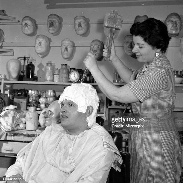 Comedian Benny Hill having a plaster cast of his skull made, so a wig can be fitted correctly. Make up girl seen here breaking the cast with a hammer...
