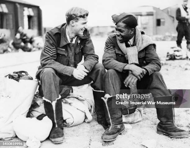Two bomber aircrew, Sergeant J Dickinson from Canada and Sergeant F Gilkes from Trinidad share a joke while waiting to board their aircraft for a...