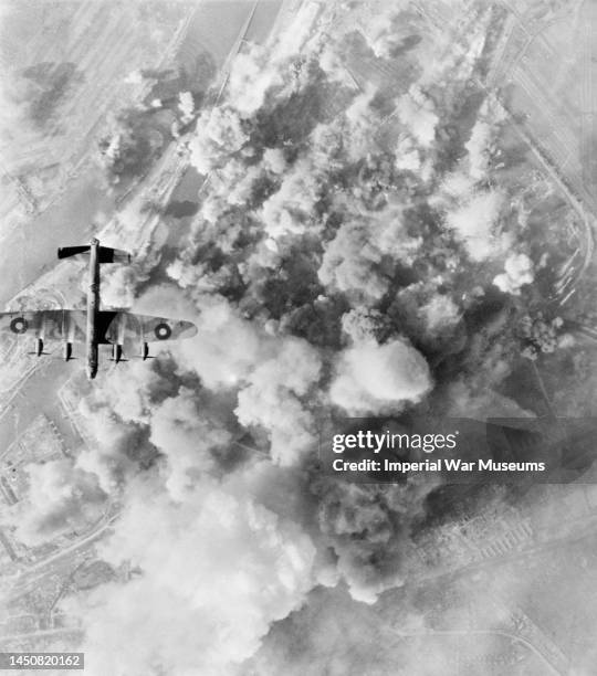 An Avro Lancaster of No 300 Polish Bomber Squadron flying over the smoke-covered target area during a daylight attack on the oil refinery and storage...