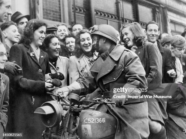 Dispatch rider from the 1st Polish Armoured Division with a local girl as passenger, is greeted by happy townspeople liberated by the Poles from...