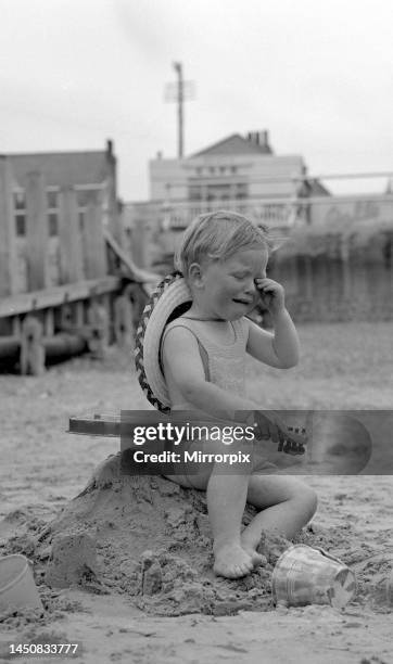 Small boy tired and over excited sitting on the remains of his sand castles crying during the May Bank Holiday sunshine whilst his little sister...