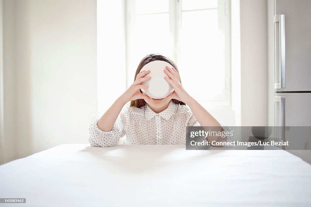 Girl drinking from bowl at kitchen table