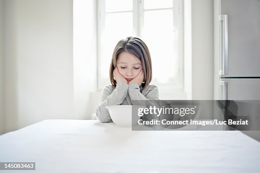 Girl examining empty bowl at table Girl examining empty bowl at table
