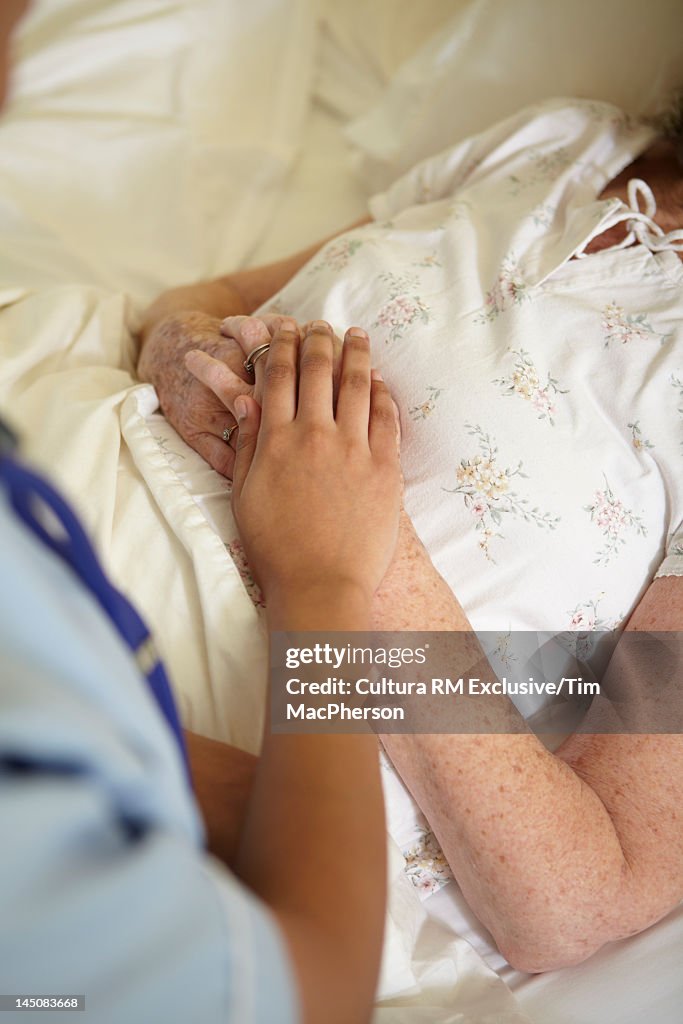Nurse holding older womans hands in bed