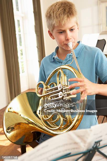 boy playing french horn at home - blaasinstrument stockfoto's en -beelden