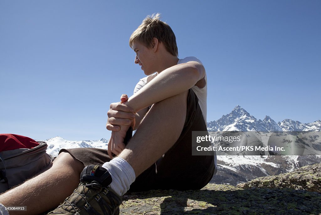 Teen hiker sits on rock above mtns, looking out