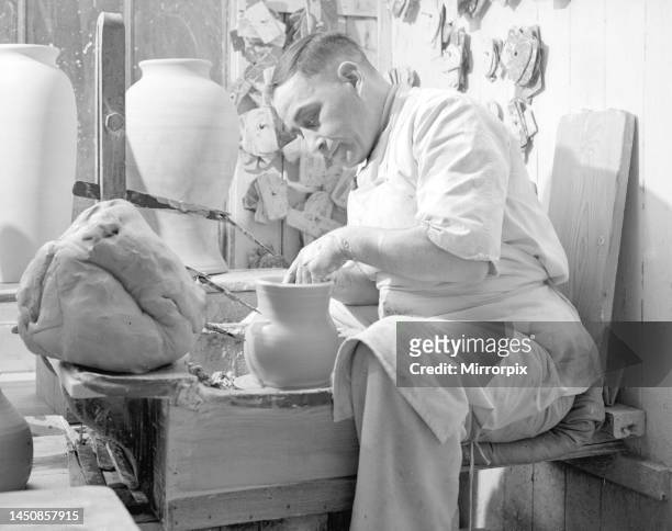 Potter sits at his potters wheel and throws a pot. Circa 1930.