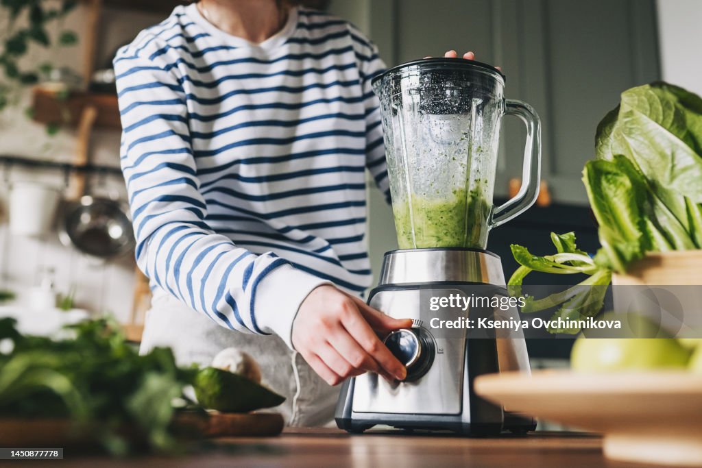 Healthy eating, cooking, vegetarian food, dieting and people concept - close up of young woman with blender and green vegetables making detox shake or smoothie at home
