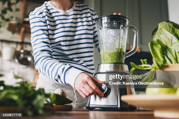 healthy eating, cooking, vegetarian food, dieting and people concept - close up of young woman with blender and green vegetables making detox shake or smoothie at home - mixer stock-fotos und bilder