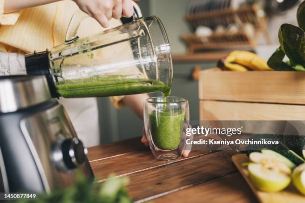 happy woman on detox diet, pouring green cocktail from mixer into glass in kitchen - milkshake stock pictures, royalty-free photos & images