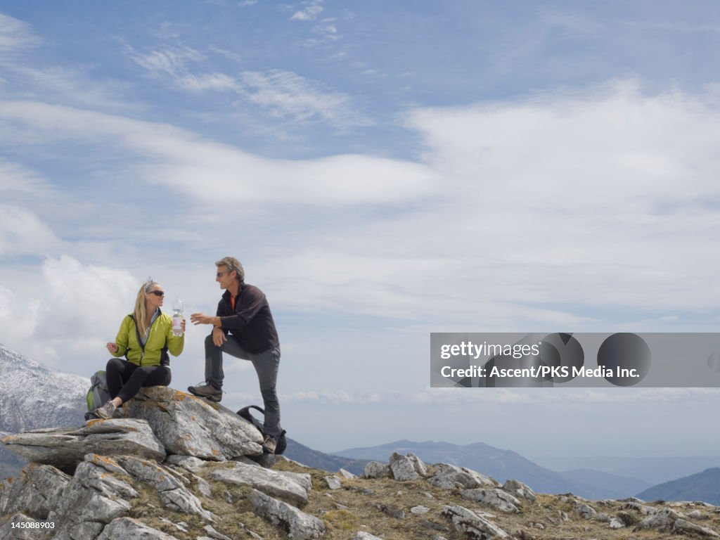 Hikers share water bottle, mountain summit