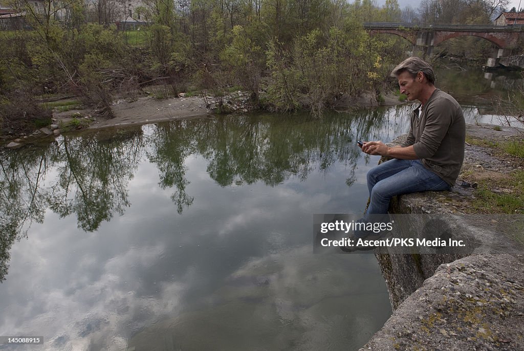 Man sends text message while perched above river