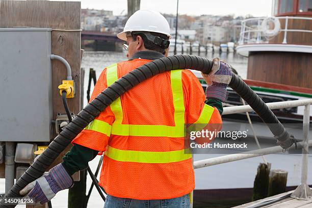 environmental engineer extending petroleum hose for toxic waste cleanup to commercial ship - industrial hose stockfoto's en -beelden