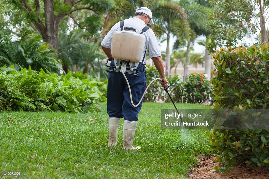 Pest control technician with portable spray rig using spray nozzle and hose