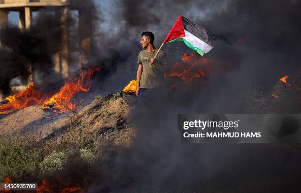 Palestinian youth holds a flag next to burning tyres during a protest by the border fence with Israel east of Gaza City on July 3, 2023. Israel has...