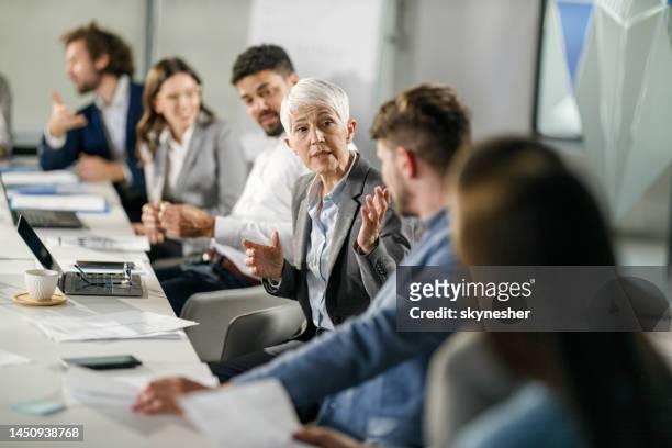 senior businesswoman talking to her colleagues in the office. - board room stock pictures, royalty-free photos & images
